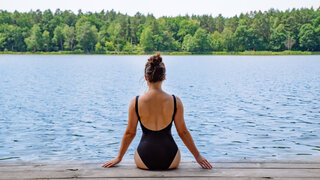 Frau sitzt auf einem Steg am See