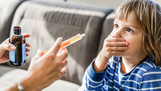 Ein Kind hält sich den Mund zu, während die Mutter eine gefüllte Spritze mit Saft in der Hand hält.