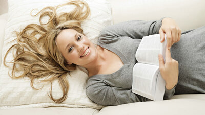 Frau liegt auf dem Sofa und liest ein Buch