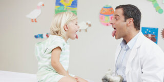 Kinderarzt  und Kind strecken die Zunge raus