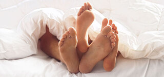 Paar liegt mit gut gepflegten Füßen im Bett