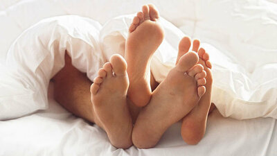 Paar liegt mit gut gepflegten Füßen im Bett