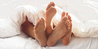 Paar liegt mit gut gepflegten Füßen im Bett