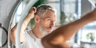 Mann untersucht seine Haare auf Kopfschuppen