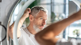 Mann untersucht seine Haare auf Kopfschuppen