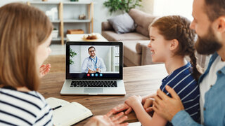 Familie schaut auf Computer mit Arzt auf dem Bildschirm