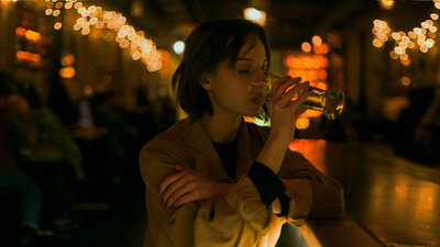 Eine Frau sitzt allein in einer Bar und trinkt Bier.
