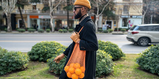 Ein Mann trägt ein Netz mit Orangen über die Schulter gehängt.