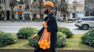 Ein Mann trägt ein Netz mit Orangen über die Schulter gehängt.