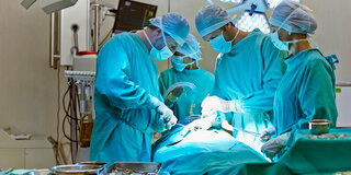 Eine Gruppe von Ärztinnen und Ärzten stehen im Krankenhaus um einen Operationstisch