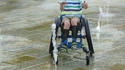 Kind im Rollstuhl fährt durch Springbrunnen