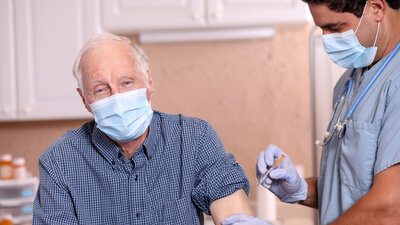 Senior mit Gesichtsmaske bei der Grippe-Impfung beim Arzt