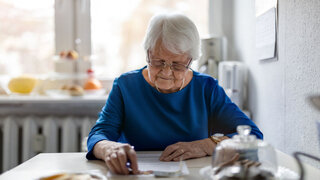 Eine Frau in blauem Shirt sitzt ab einem Tisch und beugt sich über ein Papier.
