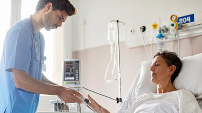 In einem Krankenhaus versorgt eine Pflegekraft eine Patientin am Bett