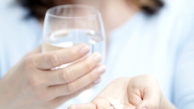 Frau nimmt Tabletten mit einem Glas Wasser ein