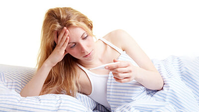 Eine Frau liest das Ergebnis einer Fiebermessung vom Thermometer ab.