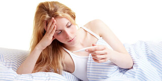 Eine Frau liest das Ergebnis einer Fiebermessung vom Thermometer ab.