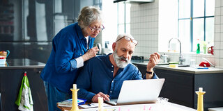 Eine  ältere Frau und ein älterer Mann sind über einen Laptop gebeugt.