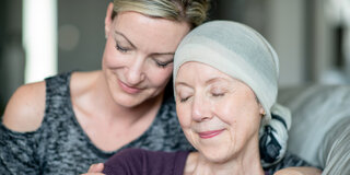 Eine Frau umarmt eine Krebspatientin, während beide die Augen geschlossen haben.