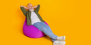 Ein Mann mit Bart lehnt sich mit geschlossenen Augen in einem Sitzsack zurück und verschränkt entspannt die Arme hinter seinem Kopf.
