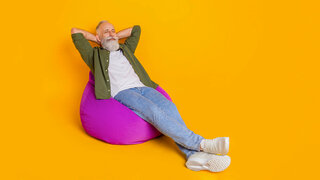 Ein Mann mit Bart lehnt sich mit geschlossenen Augen in einem Sitzsack zurück und verschränkt entspannt die Arme hinter seinem Kopf.
