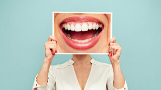 Eine Frau hält sich ein Bild vor das Gesicht, auf dem ein lachender Mund mit gesunden Zähnen zu sehen ist.