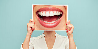 Eine Frau hält sich ein Bild vor das Gesicht, auf dem ein lachender Mund mit gesunden Zähnen zu sehen ist.