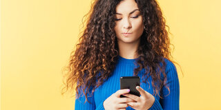 Frau stehen an Wand skeptisch auf Smartphone schauen Locken Influencer Medizin Nachdenklich Mimik