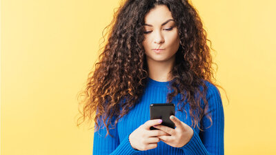 Frau stehen an Wand skeptisch auf Smartphone schauen Locken Influencer Medizin Nachdenklich Mimik