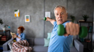Ein Mann im blauen T-Shirt trainiert mit Handhanteln und blickt dabei auf seine linke Hand.