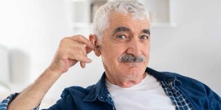 Ein Mann setzt sein Hörgerät ins Ohr.