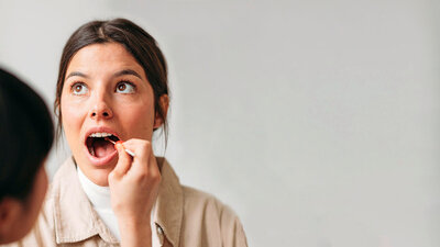 Eine Ärztin nimmt bei einer Patientin aus dem geöffneten Mund einen Rachenabstrich.