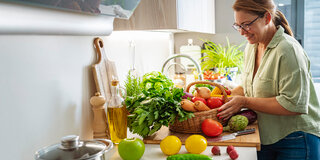 Eine Frau packt in ihrer Küche die Einkäufe aus, darunter verschiedene Gemüse und Obst.