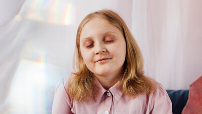Ein Mädchen mit schulterlangen blonden Haaren hält die Augen geschlossen.