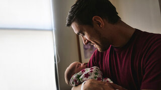 Ein junger Vater hält sein neugeborenes Kind im Arm.
