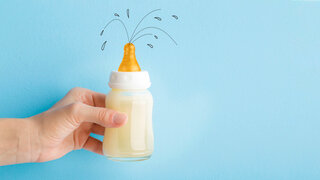 Eine Illustration zeigt ein Baby-Fläschen, aus dem einige Spritzer Milch herausspritzen.