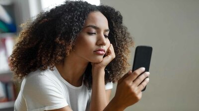 Eine junge Frau hält ein Smartphone in der Hand und blickt schlecht gelaunt auf dessen Bildschirm.