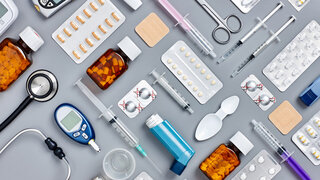 Auf einem Tisch sind verschiedene Gegenstände aus einer Apotheke wie Spritzen, Tabletten und Blutzuckermessgeräte angeordnet.