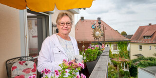 Sabine Graf steht auf dem Balkon ihrer Wohnung und hält einen Kaffeebecher in der Hand.