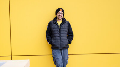 Daniel Saunders lehnt an einer gelben Wand.