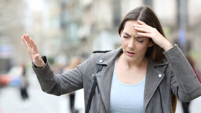 Eine Frau hält eine Hand an den Kopf, weil sie sich unwohl fühlt.