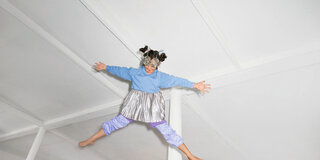 Ein Mädchen mit einer Maske aus Küchensieben springt in die Luft und streckt fröhlich lachend die Arme und Beine aus.