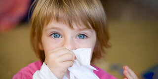 Ein Kind putzt sich mit einem Papiertaschentuch die Nase.
