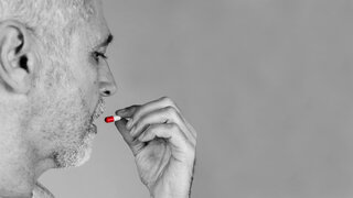 Ein älterer Mann führt eine Medikamentenkapsel zum Mund, um sie einzunehmen.