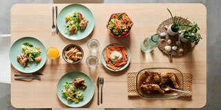 Auf einem Tisch sind drei Teller gedeckt, auf denen Salat und Hühnchen angerichtet sind.