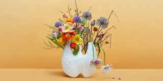 In einer Vase in Form einer Schilddrüse stehen Blumen, von denen einige schlapp herunterhängen.