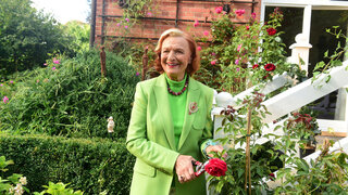 Brigitte Antonius steht im Garten neben einem Rosenbusch.