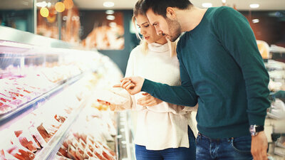Ein Mann und eine Frau stehen an einer Fleischtheke und prüfen das Angebot genau.