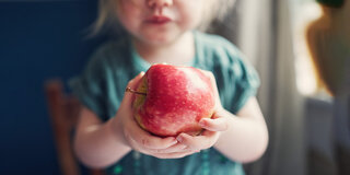 Ein Kleinkind hält mit beiden Händen einen roten Apfel.
