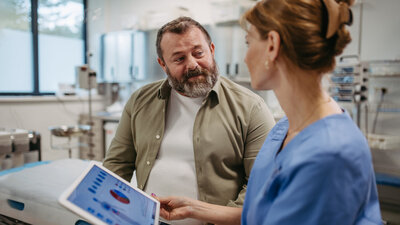 Eine Ärztin spricht mit einem adipösen Mann und hält dabei ein Tablet mit Gesundheitsdaten in der Hand.